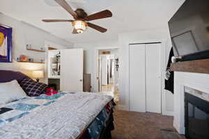 Bedroom featuring carpet floors, a ceiling fan, a closet, and a glass covered fireplace