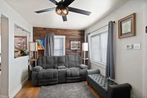 Living room with baseboards, a ceiling fan, an accent wall, wood finished floors, and wood walls