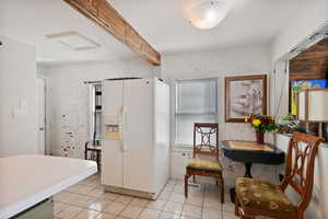 Kitchen featuring white refrigerator with ice dispenser, brick wall, beam ceiling, and light tile patterned floors