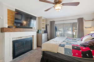 Bedroom featuring a fireplace with flush hearth, ceiling fan, and wood finished floors