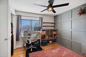 Office space with light wood-style floors, ceiling fan, and a decorative wall