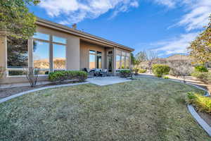 Rear view of house with stucco siding, a yard, and a patio