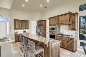 Kitchen with light stone counters, visible vents, a towering ceiling, appliances with stainless steel finishes, and premium range hood