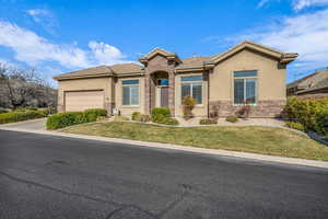 View of front of home with an attached garage, a tile roof, stone siding, stucco siding, and a front lawn