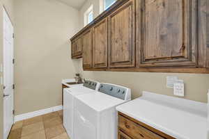 Washroom featuring light tile patterned floors, cabinet space, a sink, washer and dryer, and baseboards