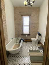 Full bathroom featuring an inviting chandelier, a freestanding bath, toilet, and tile patterned floors