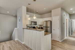 Kitchen with light wood finished floors, dark stone counters, white cabinets, appliances with stainless steel finishes, and a peninsula