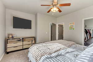 Bedroom with ceiling fan, light carpet, baseboards, a closet, and a walk in closet