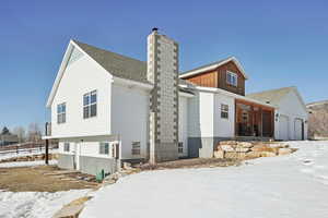 Snow covered property featuring a garage, a shingled roof, and a chimney