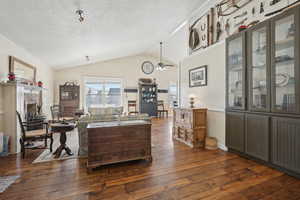 Living room featuring dark wood finished floors, a fireplace, lofted ceiling, a ceiling fan, and a textured ceiling