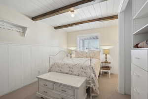 Bedroom featuring wainscoting, beamed ceiling, and light carpet