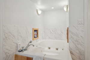 Full bathroom with a tub with jets and tile walls