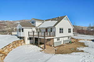 Snow covered back of property featuring a deck with mountain view and roof with shingles