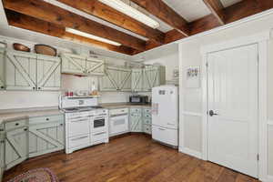 Kitchen featuring dark wood-style floors, stainless steel microwave, fridge, double oven range, and beam ceiling