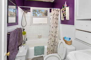 Bathroom with toilet, shower / tub combo with curtain, and wainscoting