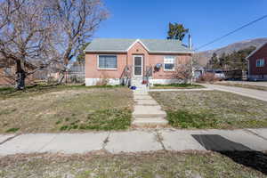 Bungalow-style house featuring a shingled roof, brick siding, and a front lawn