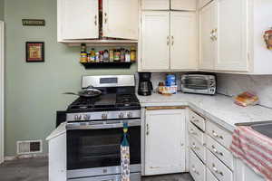 Kitchen featuring a toaster, light countertops, visible vents, stainless steel gas stove, and white cabinets