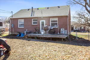 Rear view of property with a shingled roof, brick siding, fence, and a wooden deck