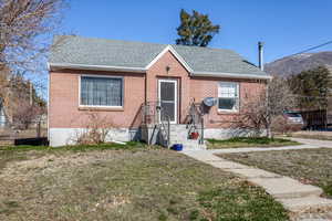 Bungalow-style house with brick siding, roof with shingles, a front lawn, and fence