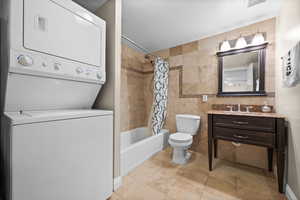 Full bath with toilet, shower / bath combination with curtain, vanity, stacked washing maching and dryer, and tile walls