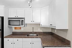 Kitchen featuring a sink, white cabinetry, appliances with stainless steel finishes, dark countertops, and rail lighting