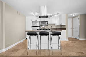 Kitchen with island range hood, stainless steel appliances, white cabinets, dark countertops, and a kitchen bar