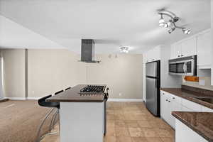 Kitchen featuring stainless steel appliances, white cabinets, a kitchen island, and wall chimney exhaust hood