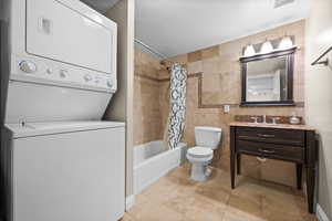 Full bath featuring visible vents, toilet, shower / tub combo with curtain, stacked washing maching and dryer, and tile walls