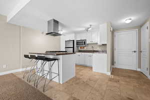 Kitchen featuring dark countertops, appliances with stainless steel finishes, a breakfast bar, range hood, and a sink