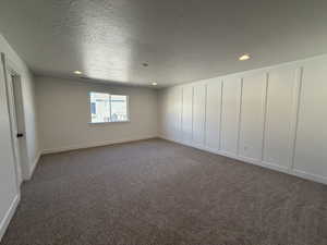 Empty room featuring a textured ceiling, carpet floors, recessed lighting, and a decorative wall