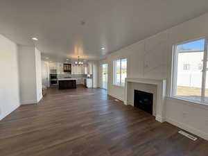 Unfurnished living room featuring a brick fireplace, visible vents, dark wood finished floors, and a notable chandelier