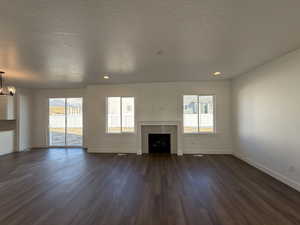 Unfurnished living room with dark wood-style flooring, a notable chandelier, a fireplace, and baseboards