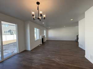 Unfurnished room with a chandelier, dark wood finished floors, a fireplace, and baseboards