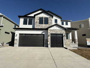 View of front of house featuring an attached garage, stone siding, driveway, and board and batten siding