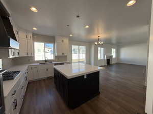 Kitchen featuring dark wood finished floors, stainless steel gas cooktop, premium range hood, white cabinetry, and a sink