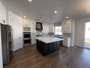 Kitchen with dark wood finished floors, light countertops, custom range hood, appliances with stainless steel finishes, and white cabinetry