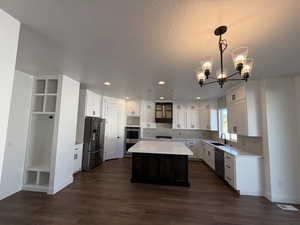 Kitchen featuring a kitchen island, a sink, white cabinets, light countertops, and appliances with stainless steel finishes