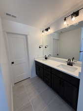 Bathroom featuring visible vents, a sink, a textured ceiling, and double vanity