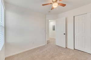 Unfurnished bedroom featuring light carpet, electric panel, baseboards, and a closet