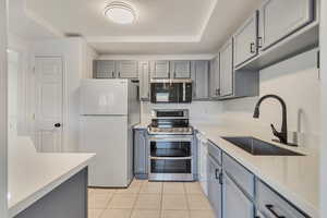 Kitchen featuring gray cabinets, stainless steel appliances, light countertops, a sink, and light tile patterned flooring