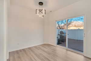 Unfurnished dining area featuring light wood-type flooring, an inviting chandelier, and baseboards