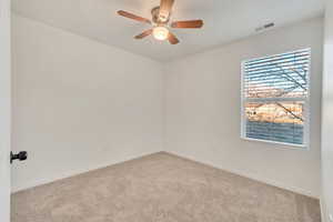 Carpeted spare room with a ceiling fan, visible vents, and baseboards