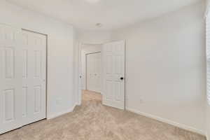 Unfurnished bedroom featuring light carpet, baseboards, and a closet