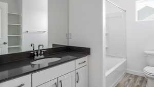 Bathroom featuring shower / washtub combination, toilet, vanity, wood finished floors, and baseboards