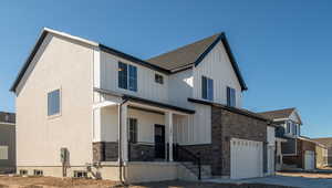 View of front of property with concrete driveway, stone siding, an attached garage, covered porch, and board and batten siding