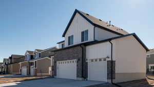 Exterior space featuring concrete driveway, stone siding, a residential view, an attached garage, and board and batten siding