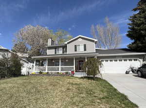 View of front of home featuring driveway, a chimney, an attached garage, covered porch, and a front lawn