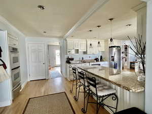 Kitchen featuring crown molding, a breakfast bar area, light wood-style flooring, appliances with stainless steel finishes, and a peninsula