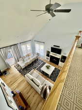 Living area featuring high vaulted ceiling, a warm lit fireplace, ceiling fan, and wood finished floors