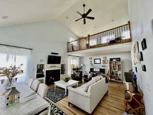 Living area with a warm lit fireplace, a healthy amount of sunlight, a ceiling fan, and light wood-style floors